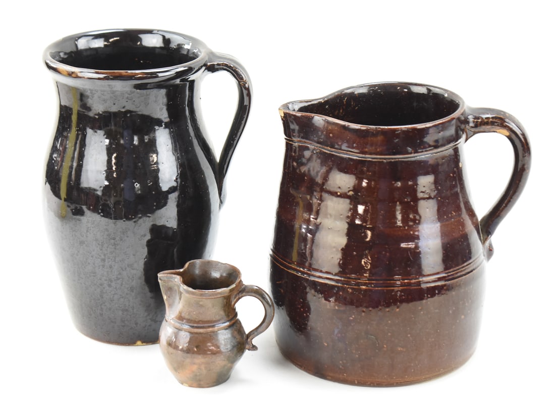 ALBANY SLIP GLAZE STONEWARE: PITCHERS AND CREAMER: This lot includes two stoneware pitchers and one creamer in Albany slip glaze, from the late 19th-early 20th century. The largest item measures approx. 10" H x 7" W x 6" D.