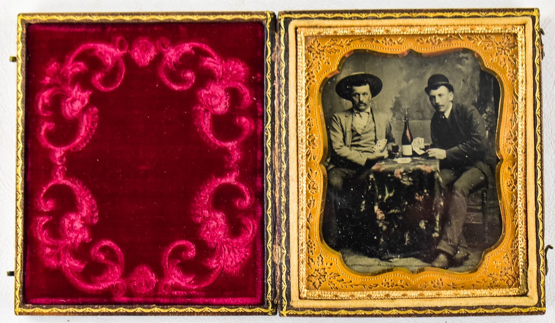 CASED TINTYPE OF MEN PLAYING CARDS: A cased tintype photograph depicting two men drinking and playing a game of cards, late 19th century. The photograph in the case measures approximately 3.5" H x 3.25" W x 0.5" W.