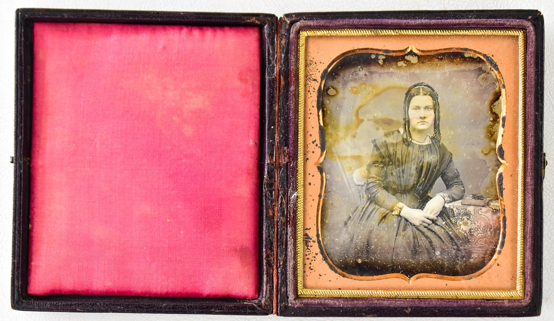 DAGUERREOTYPE PORTRAIT OF A WOMAN: A 1/6 plate daguerreotype of a woman dressed in black, mid-19th century. The outside case design is centered around a lyre and still has its original bindings. Case measures approximately 4" H x 