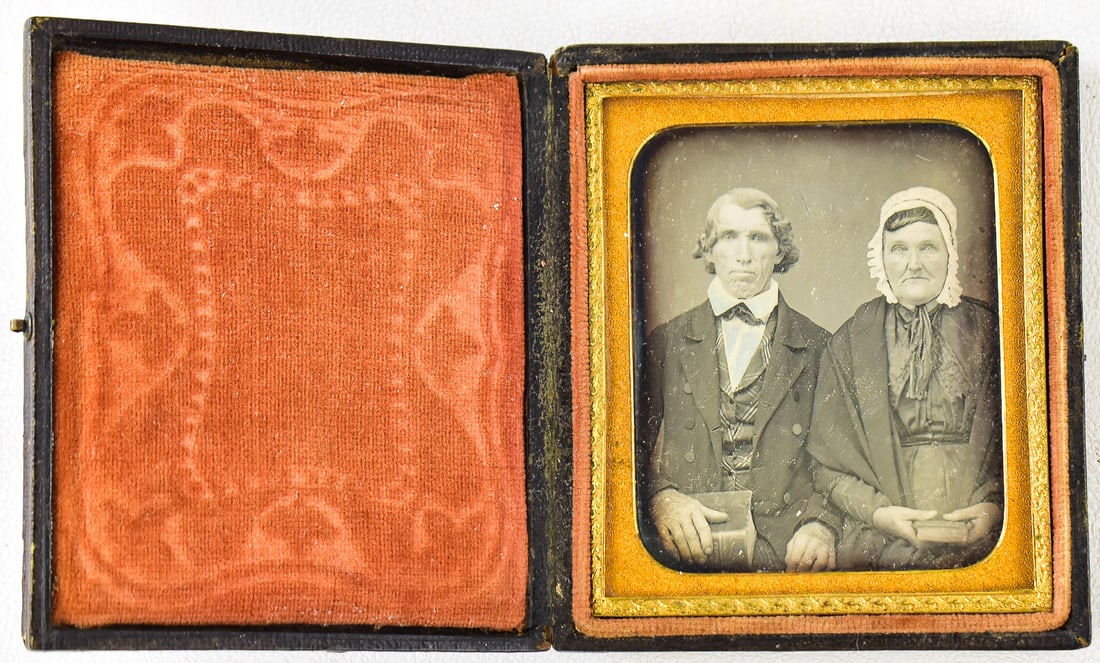 DAGUERREOTYPE OF A LITERATE COUPLE WITH THEIR BOOKS: This daguerreotype is of a man and woman with their books (likely religious literature to show literacy and piety) in a leather 1/6th plate case featuring a "Bouquet of Roses" pattern, circa 1850s.