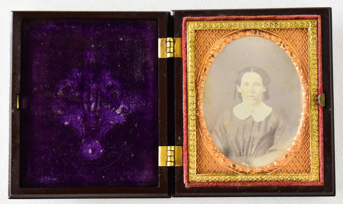 DAGUERREOTYPE OF A WOMAN IN WHITE; S. PECK & COMPANY: A S. Peck & Company (New Haven, CT) 1/9th plate case in a "Angel Carrying Babies" design with a daguerreotype is of a woman in a white collar with a stern expression, circa 1850s. The case measures