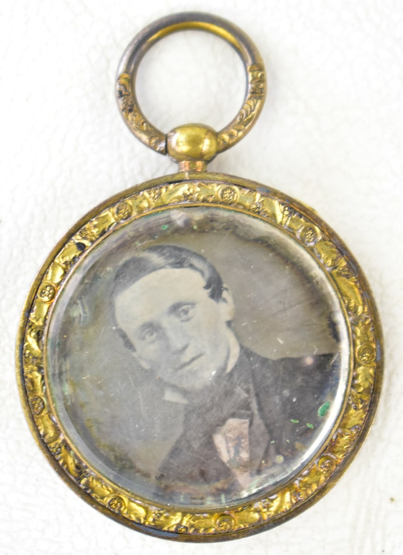 VICTORIAN PHOTOGRAPHIC PORTRAIT LOCKET FOB: A photographic portrait locket fob depicting a portrait of a young boy from the late 19th century, specifically a daguerreotype photo. The locket is composed of a silver metal oval frame with a