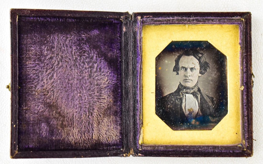PURPLE VELVET DAGUERREOTYPE: A daguerreotype featuring a man's portrait in a leather 1/9th plate case, circa 1840-1850s. Case measures approximately 3" H x 2.5" W x 0.5" D when closed.