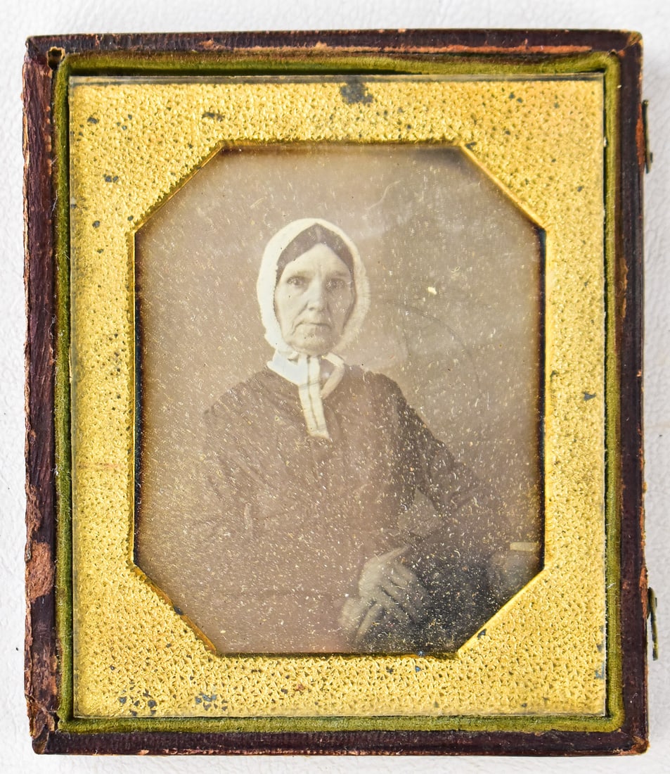 HALF-CASED DAGUERREOTYPE OF VICTORIAN-ERA WOMAN: A daguerreotype photograph of a woman wearing Victorian era attire, held in half of a photograph case; mid-19th century. The photograph measures approximately 3.5" H x 3" W x 0.5" D.