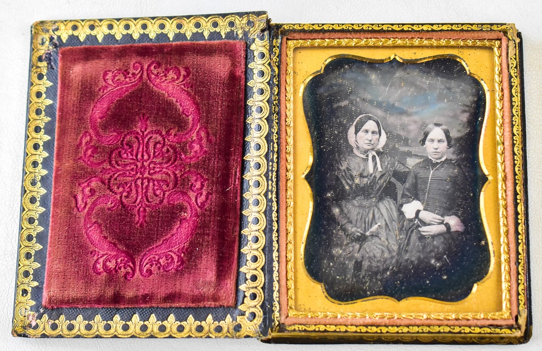 DAGUERREOTYPE IN BLACK LEATHER 1/4 BOOK PHOTOGRAPH CASE W/ MOTHER OF PEARL INLAY: A daguerreotype photograph of a mother and daughter held in a 1/4th plate black leather book photograph case with mother of pearl inlays and a red velvet interior lining, circa 1850s. The photograph