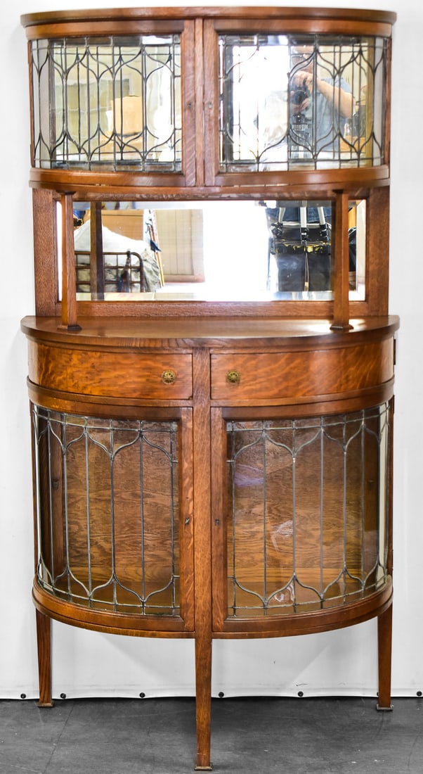 CURVED LEADED GLASS BUFFET HUTCH: This hutch has leaded glass doors on both the top and both. It is crafted in oak wood in a demilune shape with a mirror back splash. This unit does not separate into pieces and measures approx. 67" H