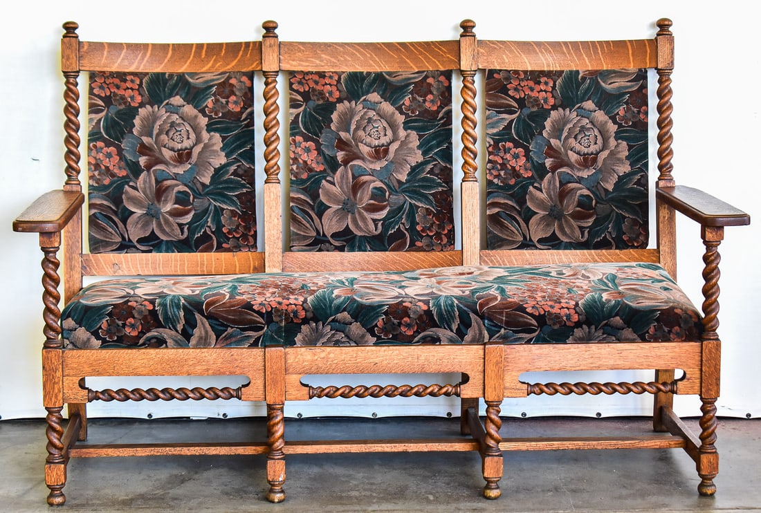 JACOBEAN REVIVAL STYLE SETTEE: This settee was crafted of quarter sawn white oak circa 1920s. It has the barley twist legs with a floral pattern upholstery. Settee measures approx. 43" H x 52.5" W x 23.5" D.
