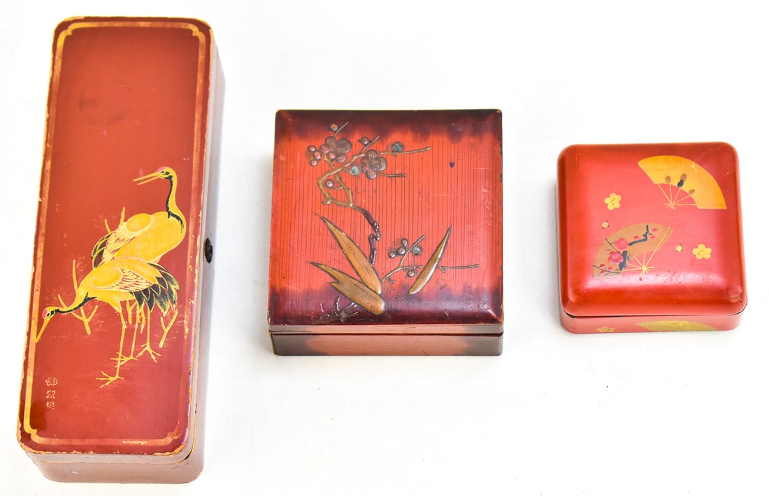 THREE JAPANESE LACQUERED WOOD BOXES: Three Japanese lacquered wood boxes with red lacquered exteriors and black lacquered interiors. The boxes have designs of cranes, Japanese hand fans, and a floral scene. The largest box measures appro