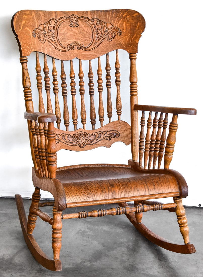 AMERICAN PRESSED BACK OAK ROCKING CHAIR: This rocking chair is crafted of oak wood circ 1900s. This chair has an ornate embossed crest and spindle backing. This chairs measures approx. 40" H x 26" W x 30.5" D.