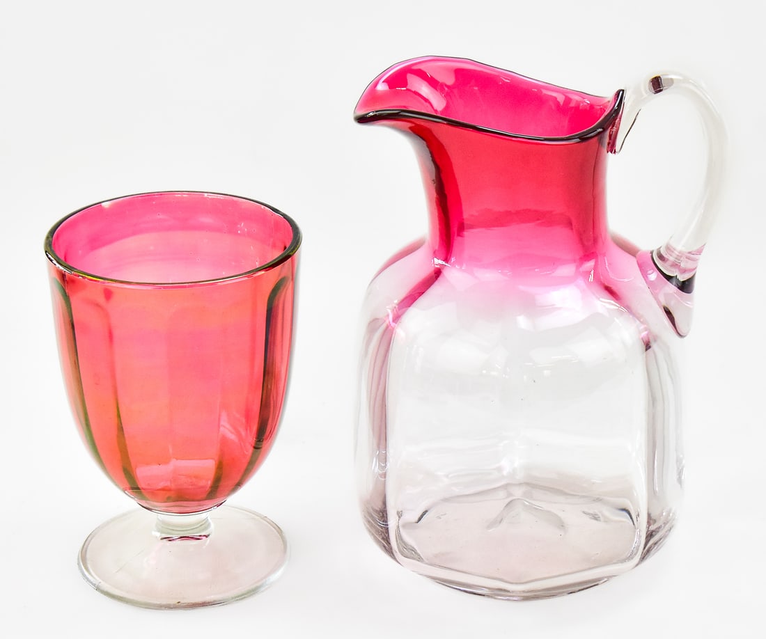 VICTORIAN HAND BLOWN CRABERRY TO CLEAR PITCHER AND GLASS: This lot consists of two hand blown cranberry to clear glass pieces. One is a gallon pitcher and the other is a 6oz glass. The pitcher measures approx. 8.5" H x 6" W x 5" D.