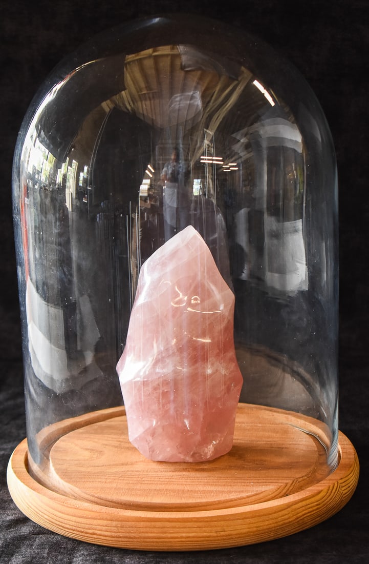 POLISHED ROSE QUARTZ FLAME CRYSTAL: Natural pink rose quartz shaped into a "crystal flame" that emphasize the stone's translucency. It is encased in a glass cloche with a wooden base. The quartz measures approx. 7" H x 4" W x 3" D, whil