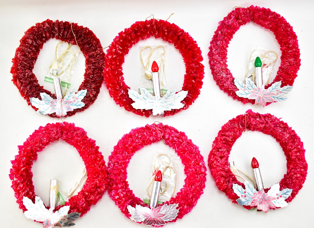 HALF DOZEN RED CELLOPHANE CHRISTMAS WREATHS: This lot has six cellophane Christmas wreaths with an electric candle in the center. They have a cardboard poinsettia accent underneath the candles. Designed to be window decorations from the