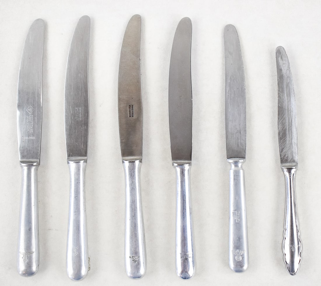 SIX GERMAN WWII LUFTWAFFE DINNER KNIVES: Six German WWII Luftwaffe dinner knives, including five standard mess hall knives and one officer's mess knife. The silverware has maker's marks, Luftwaffe markings, and Nazi Party insignias. The larg