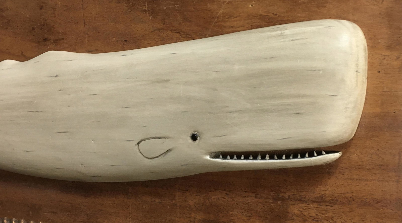 Framed White Whale Plaque by Roger Mitchell: A 12 by 34 inch wooden rope bordered frame with a hand carved and hand painted white Sperm Whale plaque by Roger Mitchell of Kingston, MA, signed with his initials under the small harpoon.In original 