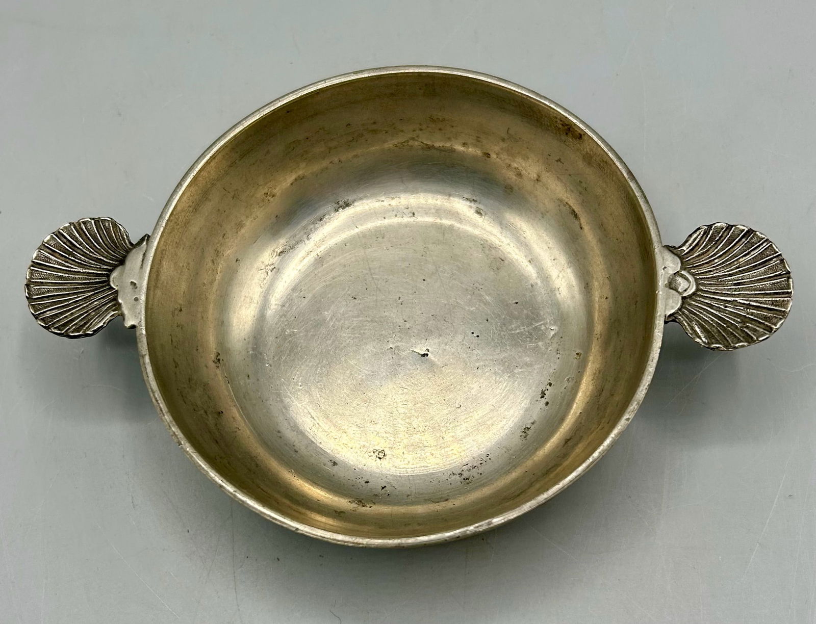 Early Pewter Porringer with Scallop Handles: A 4 5/8 diameter and 6 7/8 inches handle tip to tip pewter porringer, stamped LONDON and a crown stamp. As found- with expected wear for its age, both handle ears appeared to have been reattached.