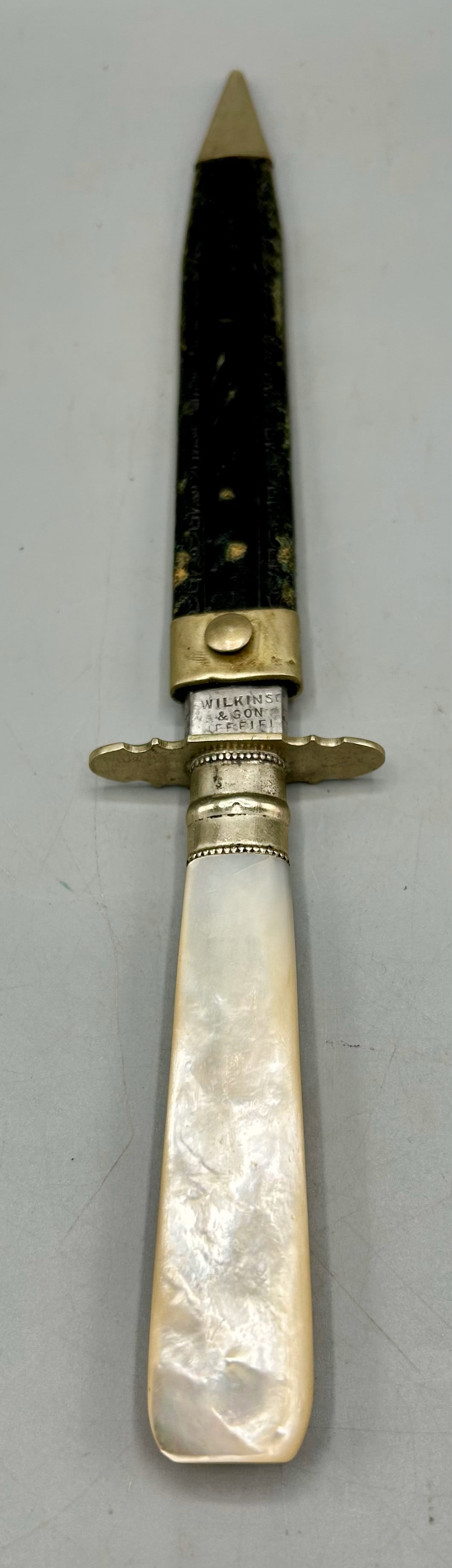 A Finely Crafted Knife by Wilkinson of Sheffield: A 10 1/2 inch highest quality knife by Wilkinson & Son with a silver band and a mother of pearl knife and a silver tipped black leather sheath. As found- with expected wear for its age.