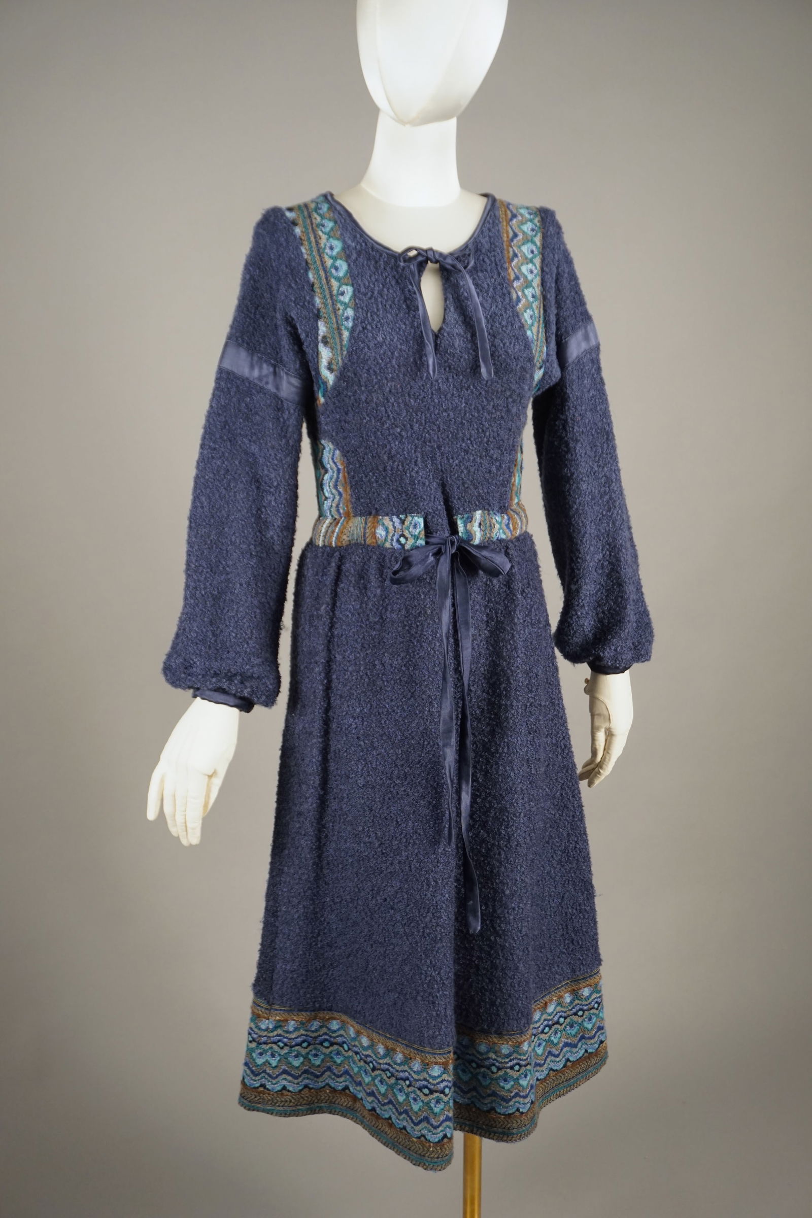 Vintage French Dauphin Toison d’Or Boucle Knit Dress: Features a luxurious bouclé wool fabric in deep navy, accented with an intricately woven jacquard trim in shades of blue, brown, and gold. The dress is lined with a smooth satin, and delicate ribbon