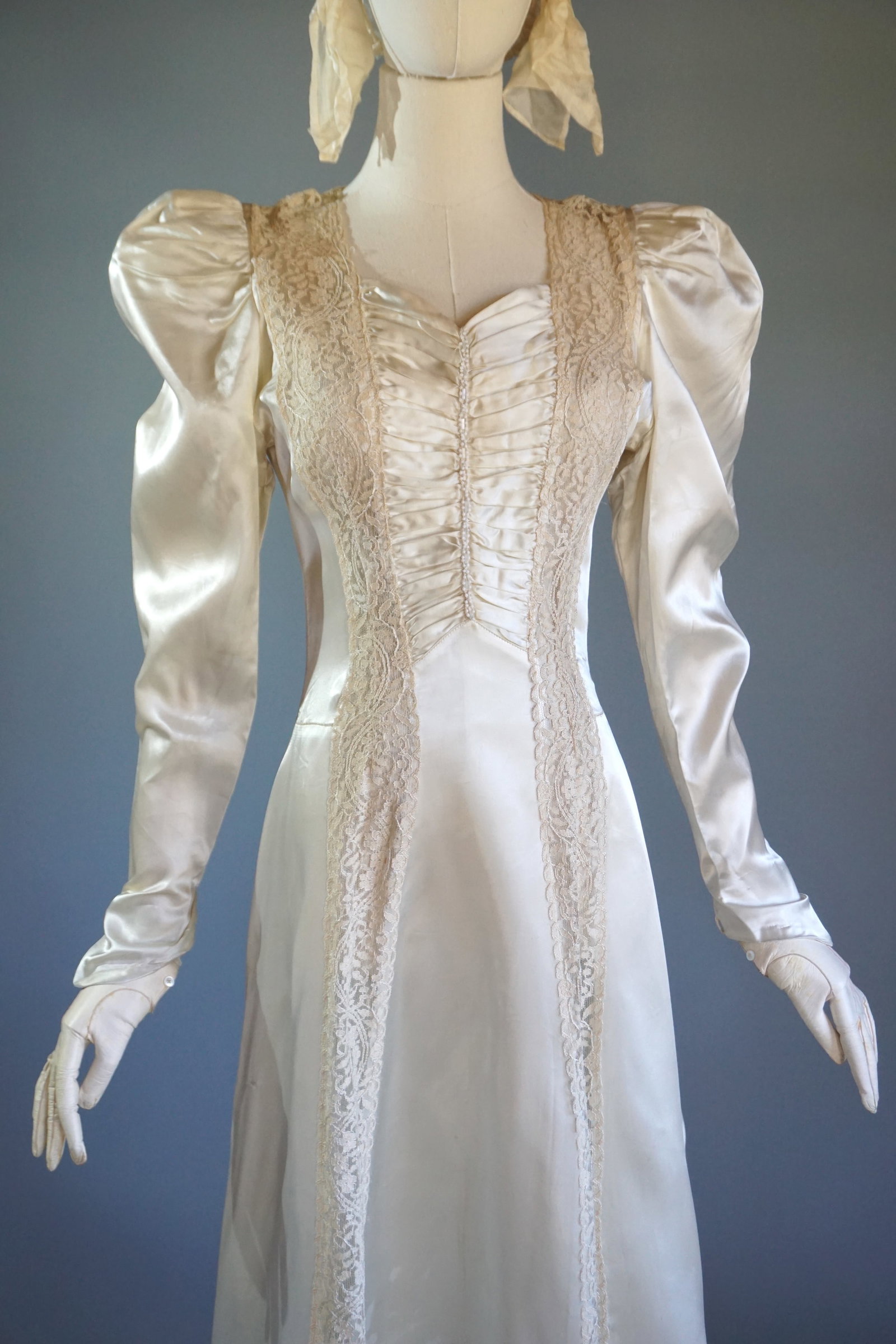 Vintage 1940s Satin Wedding Gown with Lace Panels and Cathedral Train: Vintage 1940s rayon satin wedding gown featuring intricate lace panels running down the front and extending into a dramatic cathedral-length train. The fitted bodice is adorned with ruched detailing, 