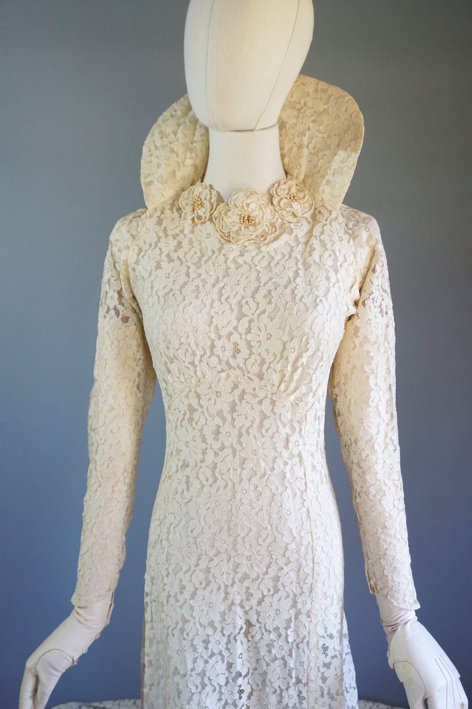 Vintage 1940s Ivory Lace Wedding Gown with High Collar & Cathedral Train: This 1940s wedding gown is crafted from delicate corded lace with embroidered floral motifs, creating a three-dimensional effect. The silhouette is fitted through the bodice, with princess seams that 