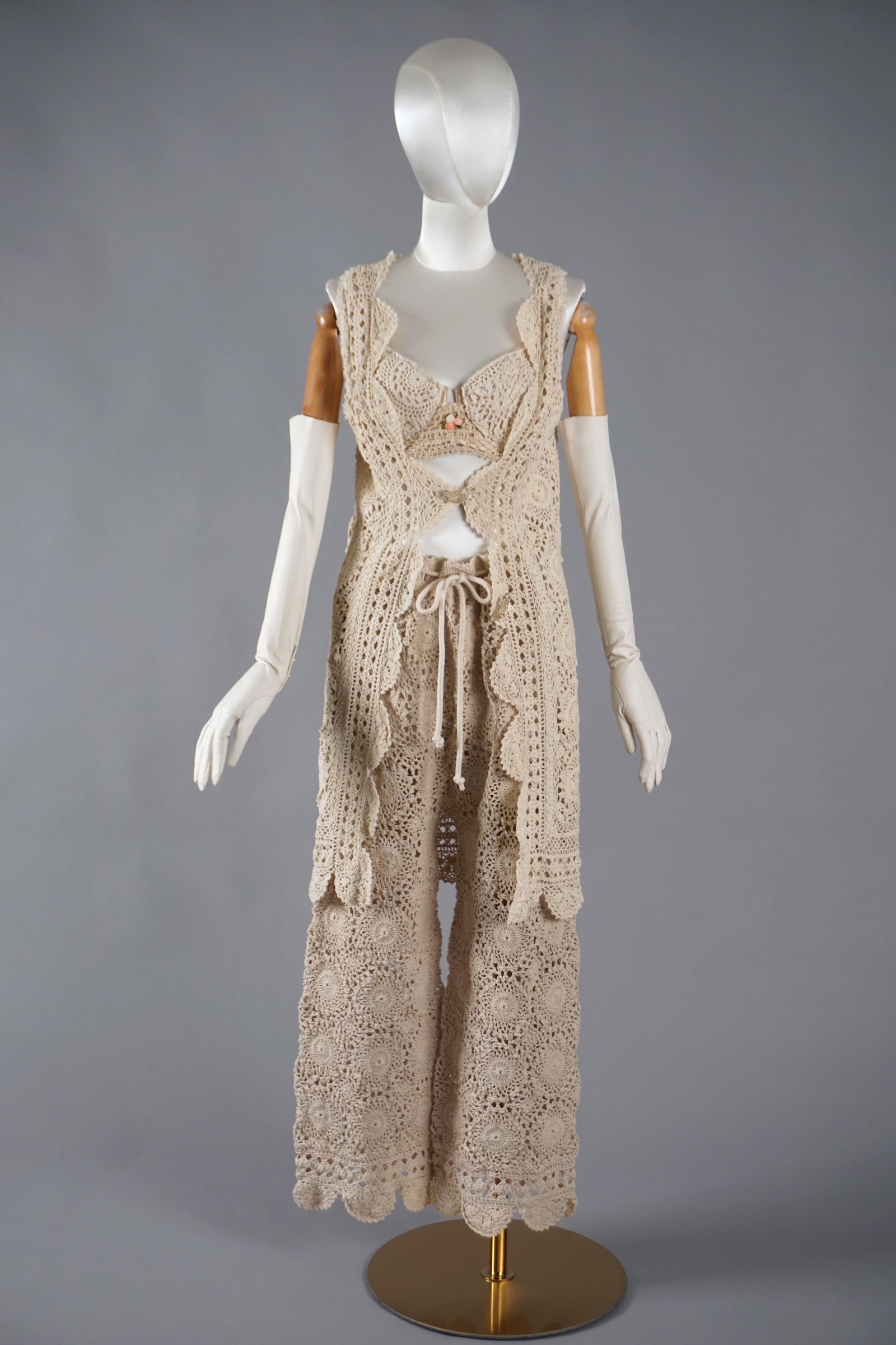 Vintage Cream Cotton Crochet Bra, Pants And Vest: A three-piece cotton crochet ensemble comprising a bra, drawstring pants, and a long vest. Made in the USA, likely late 20th century. The cream-colored crochet features circular and floral motifs thro