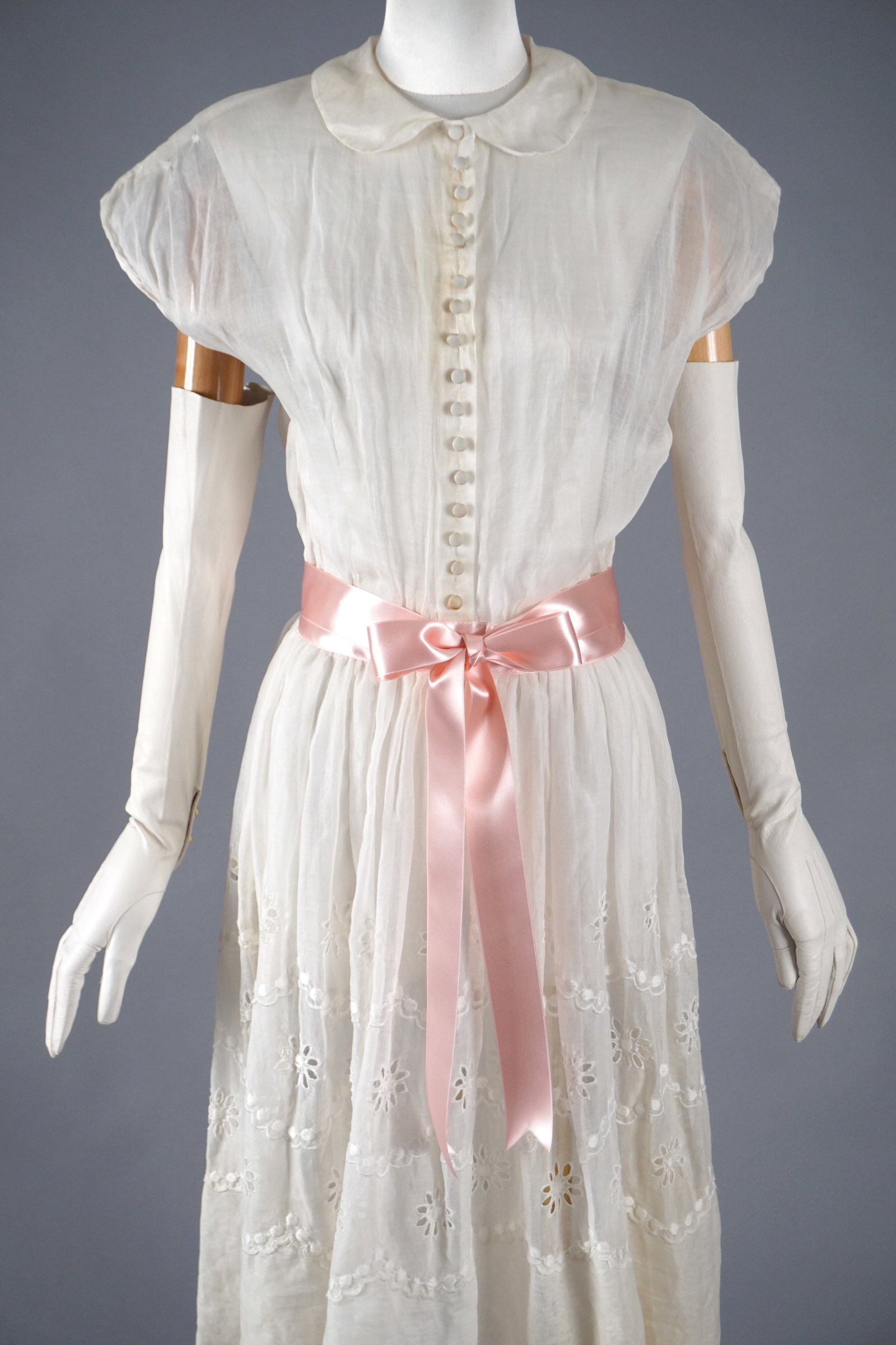 Antique Sheer Dress with Pink Satin Ribbon: Antique dress likely dating to the 1910s–1920s, made from a sheer woven fabric of organdy or fine voile. The garment features charming daisy-like eyelet embroidery across the skirt, a soft Peter Pan