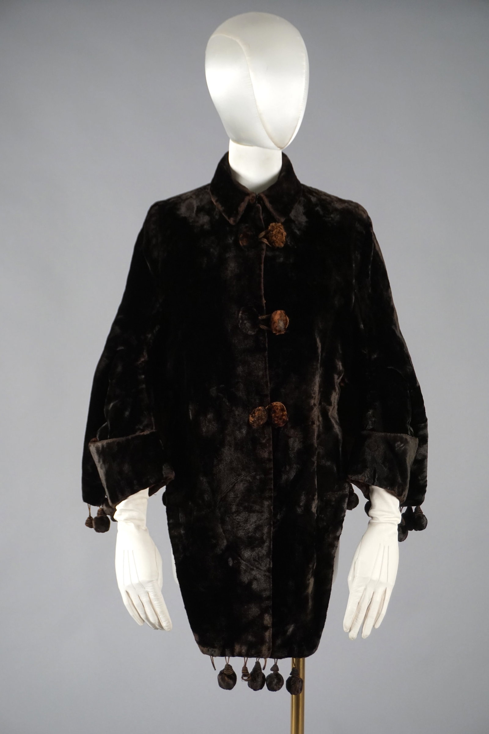 Victorian Black Velvet Fur Cape Jacket with Pom Pom Trim: Late 19th-century Victorian cape-style jacket in rich black velvet, adorned with oversized velvet-covered buttons and dramatic pom pom trim along the cuffs and hem. The loose, swing silhouette feature