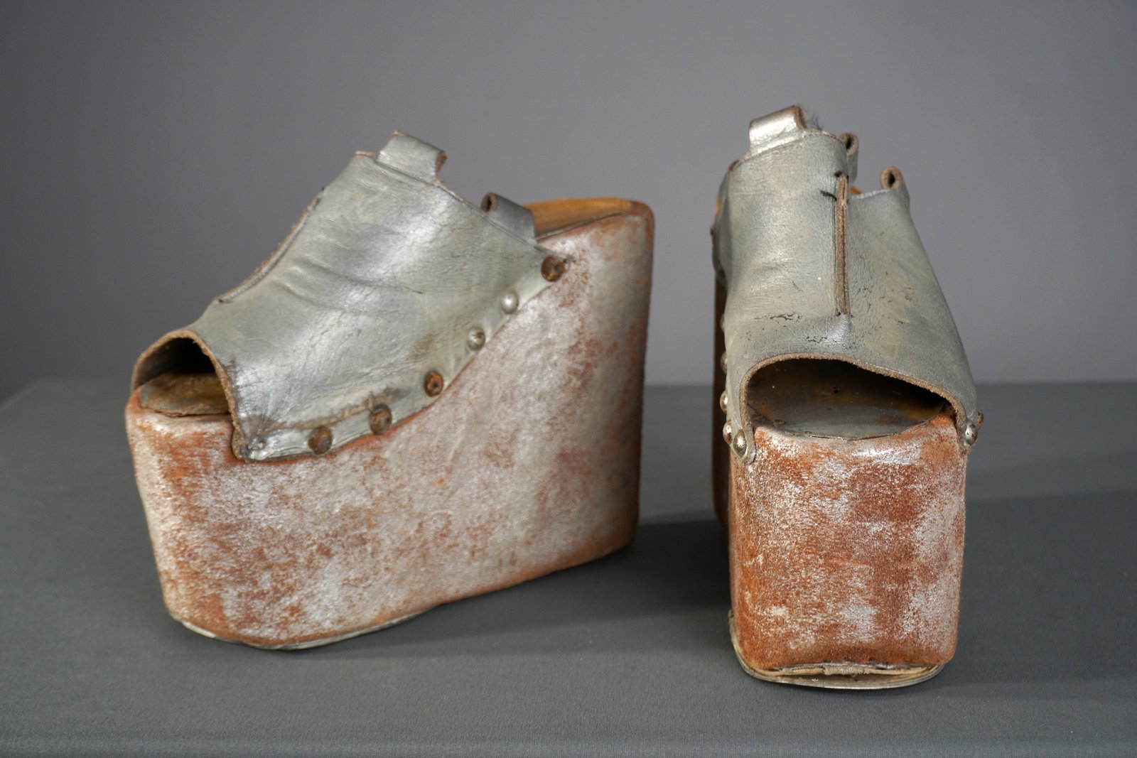 Unusual Mid-Century Theatrical Platform Shoes: A pair of heavy mid-century platform shoes, likely created for theatrical or costume use. Crafted from metallic silver leather, secured with riveted detailing. Their dramatic sculptural silhouette and