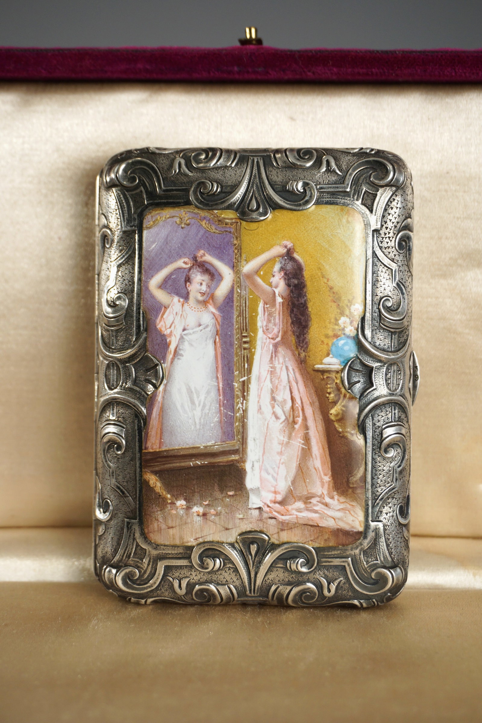 Antique Silver Enamel Erotic Cigarette Case 1904: A stunning and intimate continental silver cigarette case, dated 1904, with a richly chased rococo frame and inset hand-painted enamel plaque. The miniature scene depicts a young woman dressing before