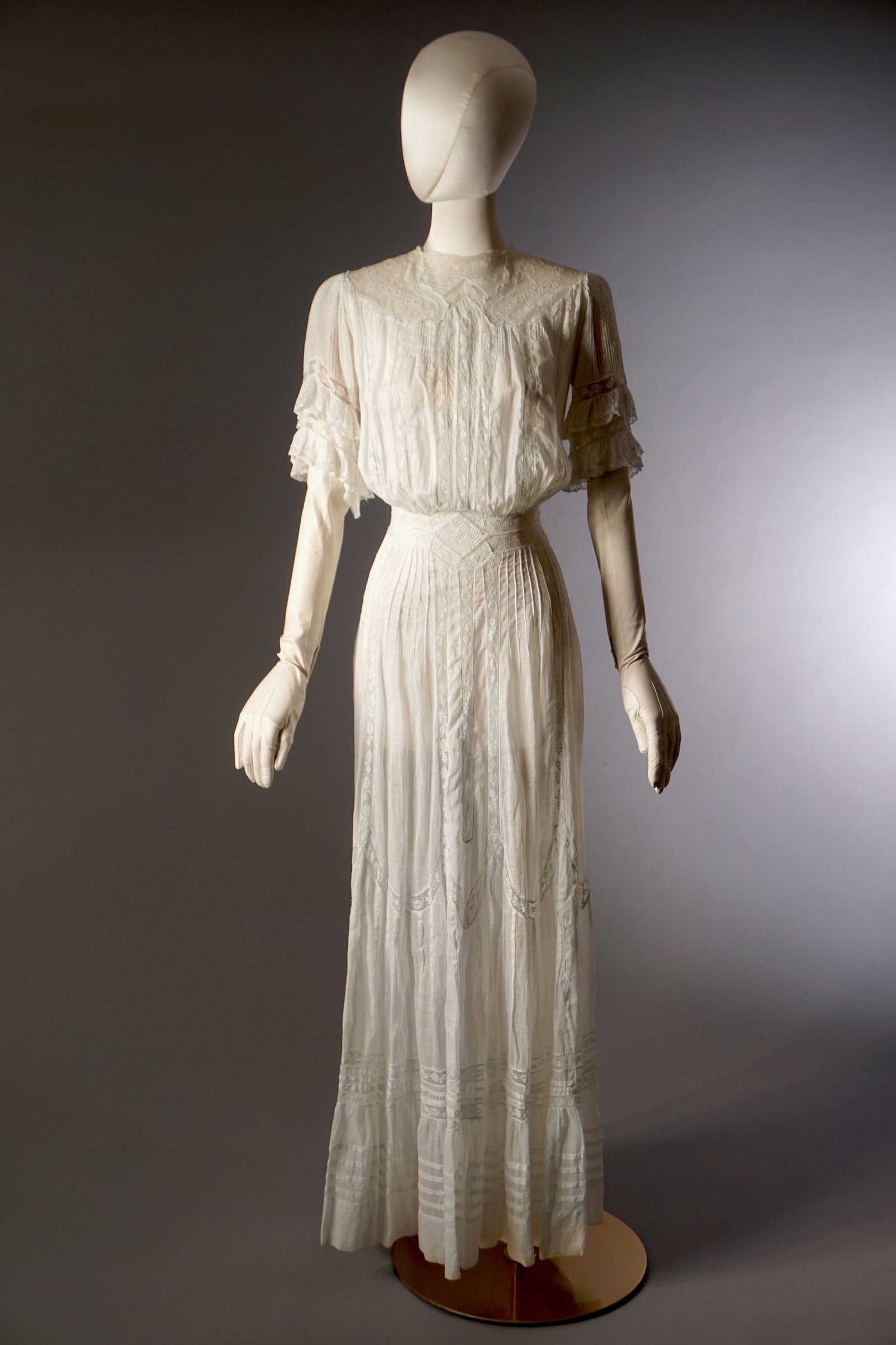 Antique Edwardian Cotton Lace Lawn Dress, c. 1905–1915: Antique white cotton lawn dress richly detailed with insertion lace, pin tucks, and ruffled sleeves. The bodice features vertical bands of lace and tiny tucks framing a high neckline with ornate lace