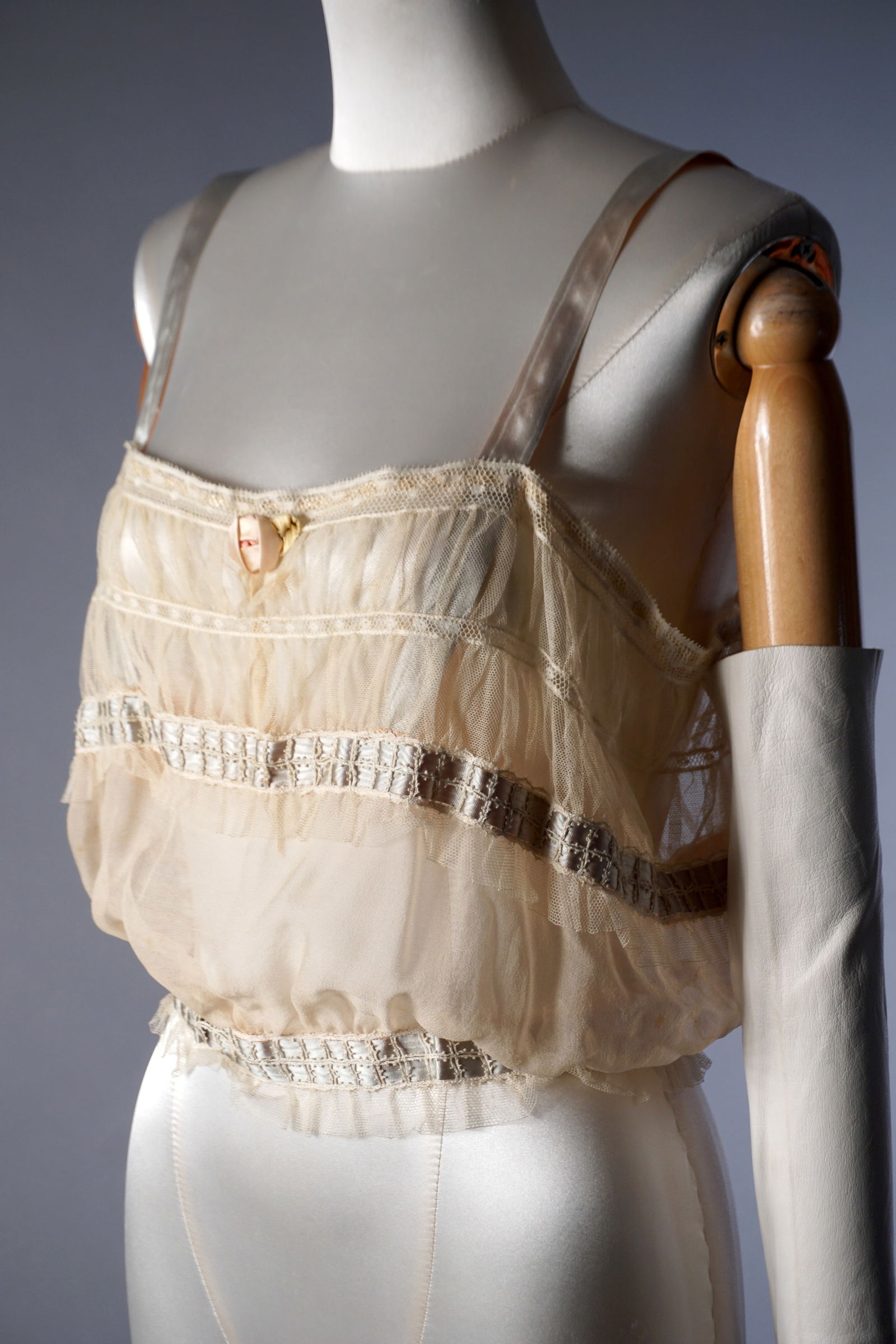 Edwardian Lace Camisole Corset Cover, c.1900–1910: Antique sheer net and lace corset cover with softly bloused silhouette, worked in horizontal bands of fine lace and insertion, and finished with a tiny shell button at the center front. Delicate pale