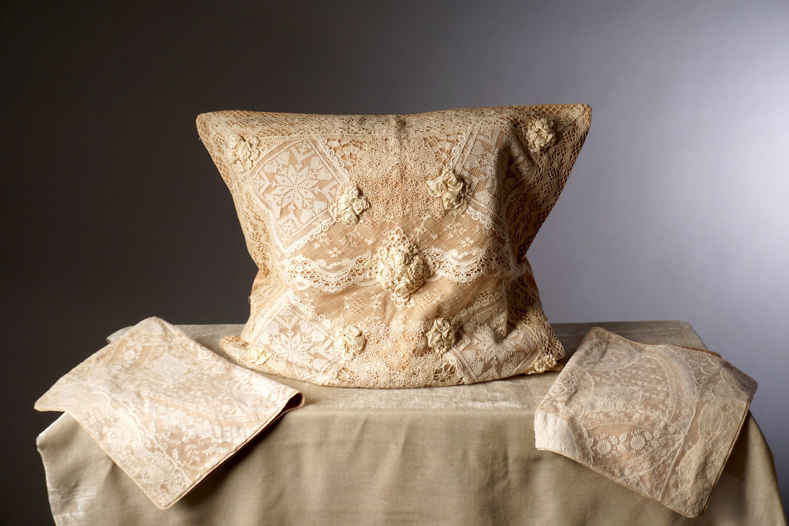 Group of Three Vintage French Cottage Lace Pillows: A trio of vintage lace pillows, including one larger square pillow and two smaller rectangular pieces. The large pillow features an intricate arrangement of mixed lace panels over a soft beige ground,