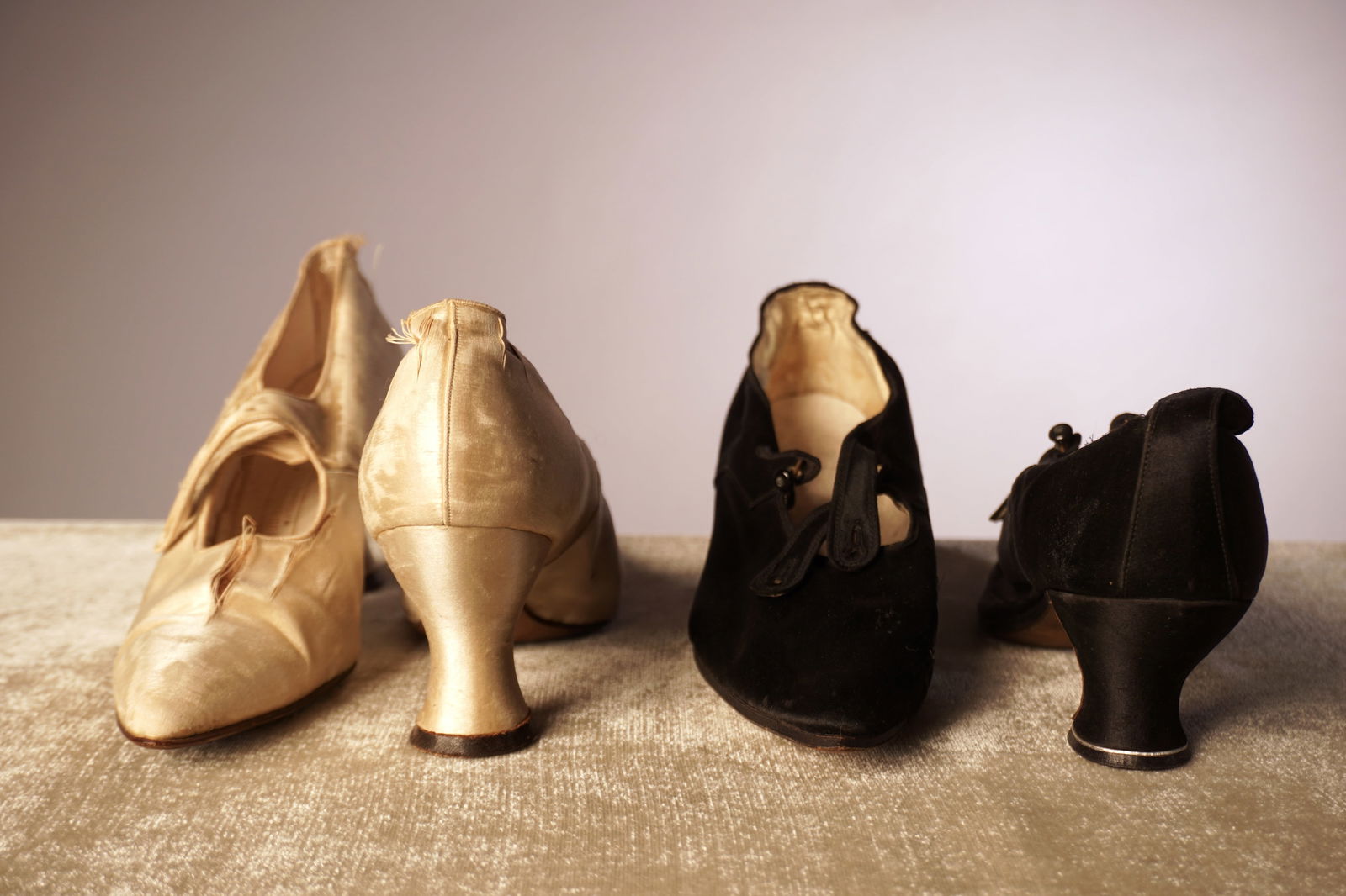 Group of Two Antique Silk Shoes: A grouping of two antique pairs of silk shoes, one in ivory satin and one in black. The ivory pair shows notable wear, fraying, and age toning consistent with delicate silk of the period. The black pa