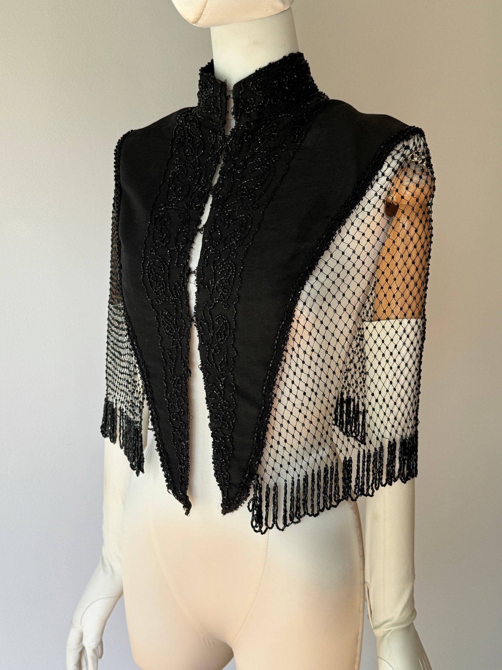 Antique Victorian Fine Glass Beaded Mourning Capelet: Late 19th century Victorian mourning capelet with intricate hand applied black glass beadwork in swirling foliate patterns across a structured black satin bodice. Dramatic open work beaded mesh sides 