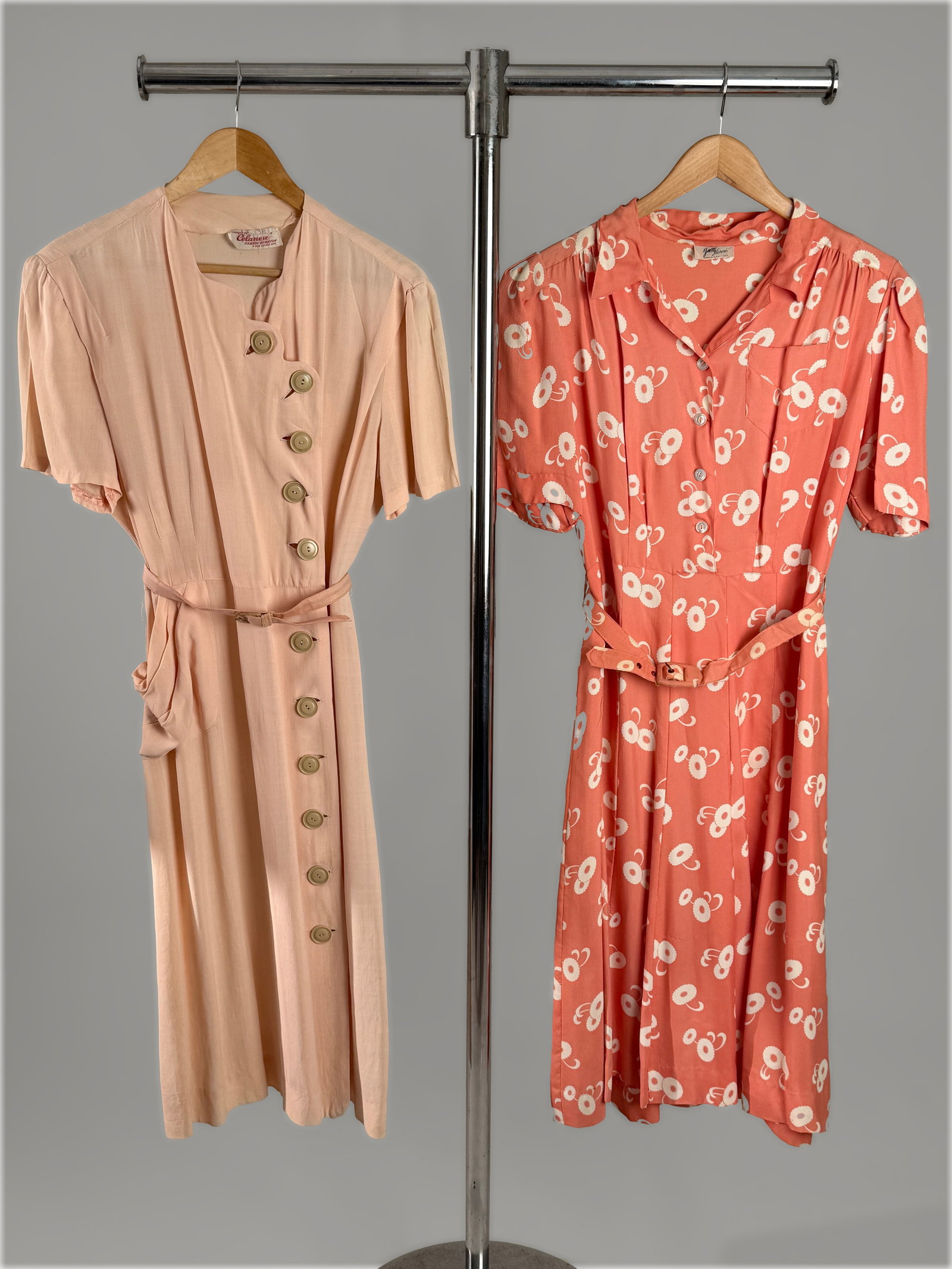 Two Vintage 1940s Pink Day Dresses with labels, Size L: Two vintage 1940s wartime day dresses. The first piece is a blush pink short sleeved dress made from Celanese rayon fabric, scalloped asymmetrical front closure with oversized buttons, belt, and a dra