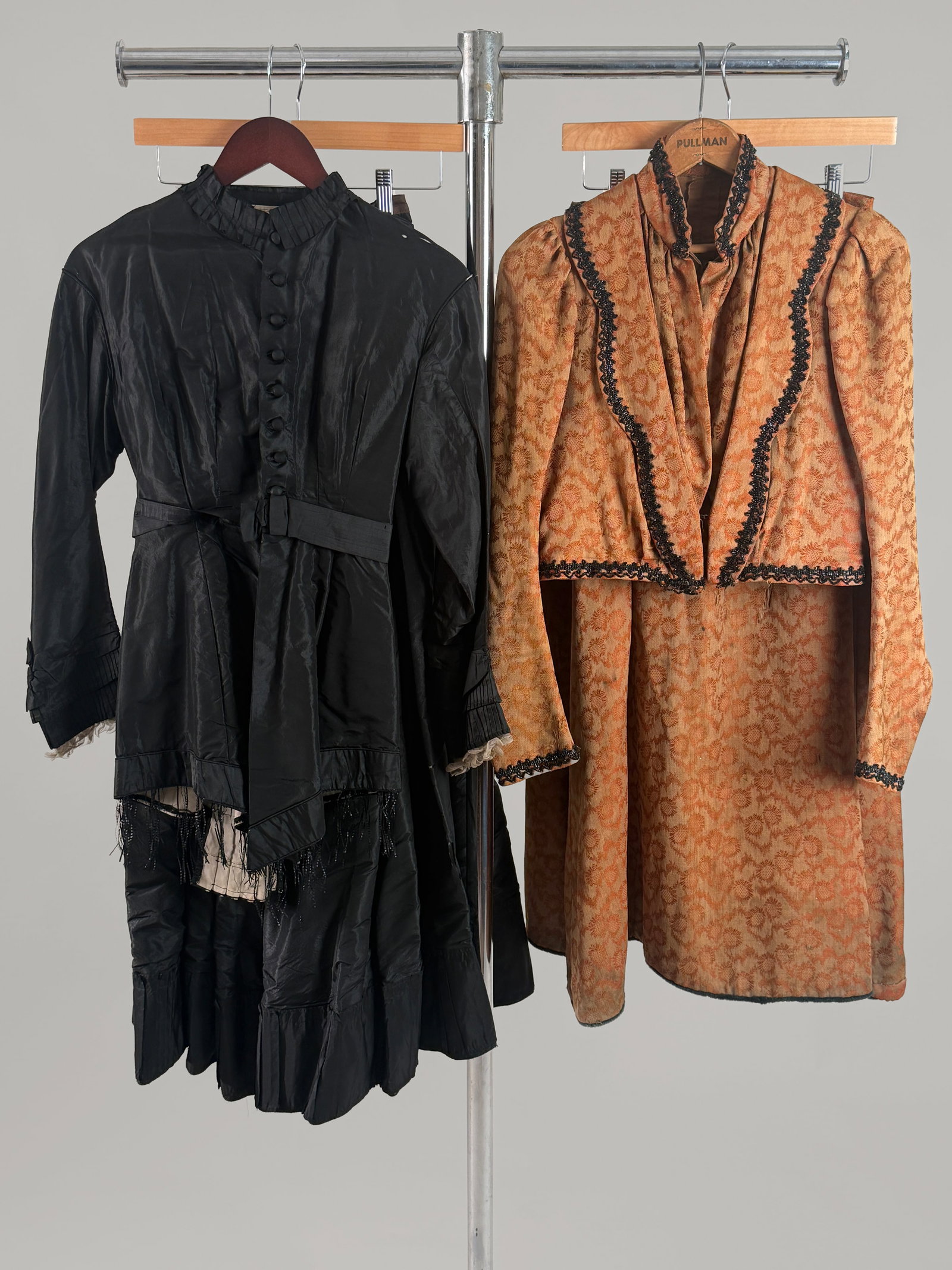 Lot of (2) Antique Victorian Women's Dresses, Black Silk and Orange Wool Print: This lot includes two antique Victorian women's garments. A two piece black silk taffeta mourning ensemble and a copper/ orange brocade ensemble with an allover woven botanical pattern and black glass