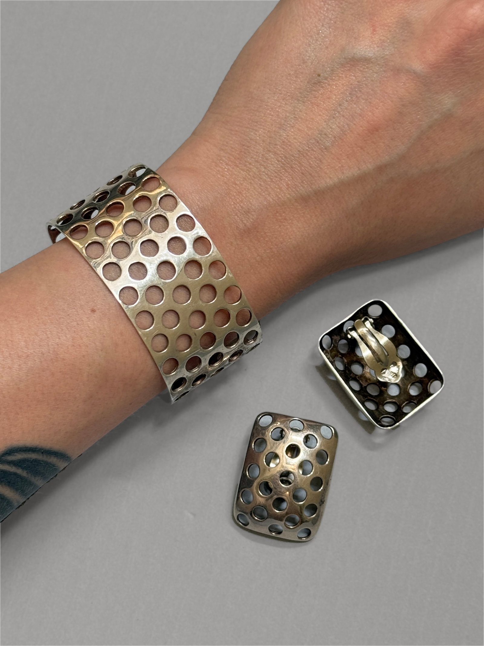 Vintage Modernist Openwork Sterling Silver Cuff and Earrings Set, Signed: Vintage modernist sterling jewelry suite showcases a minimalist, industrial openwork pattern of uniform circular cutouts on an open cuff bracelet and a pair of matching rectangular clip on earrings. S