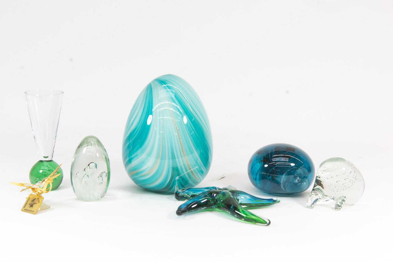 Assorted Glass Lot: This lot features (7) assorted Glass Pieces. Items include: Paperweights, Glass Egg, Starfish, Shot Glass and more. Some bases are polished and some are not. Condition Varying Conditions