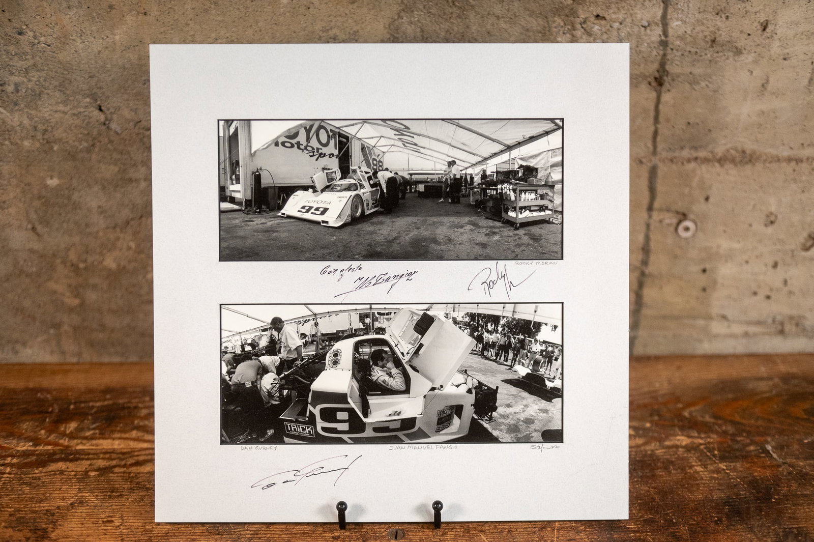 ROCKY MORAN, DAN GURNEY & JUAN MANUEL FANGIO TRIPLE SIGNED PHOTOS: Two professionally matted photos taken by master photographer, Richard Stefani circa 1990. Triple signed by racers Rocky Moran, Dan Gurney & Juan Manuel Fangio. Measures in matting, 14'' H x 14'' 