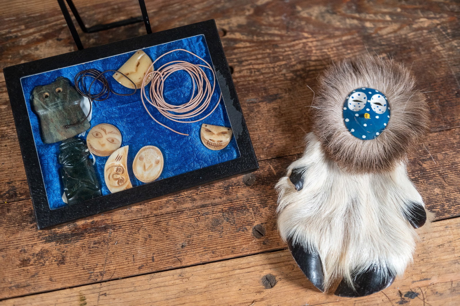BLACK COTTONWOOD MASK REINDEER DOLL BY DAVID HENDREN & NATIVE PENDANT SHADOW BOX: A doll made of a black cottonwood carved mask on a reindeer fur body, by Alaskan artist David L. Hendren. Details about the item and artist on the back of the doll. Additionally, a small shadow box wi