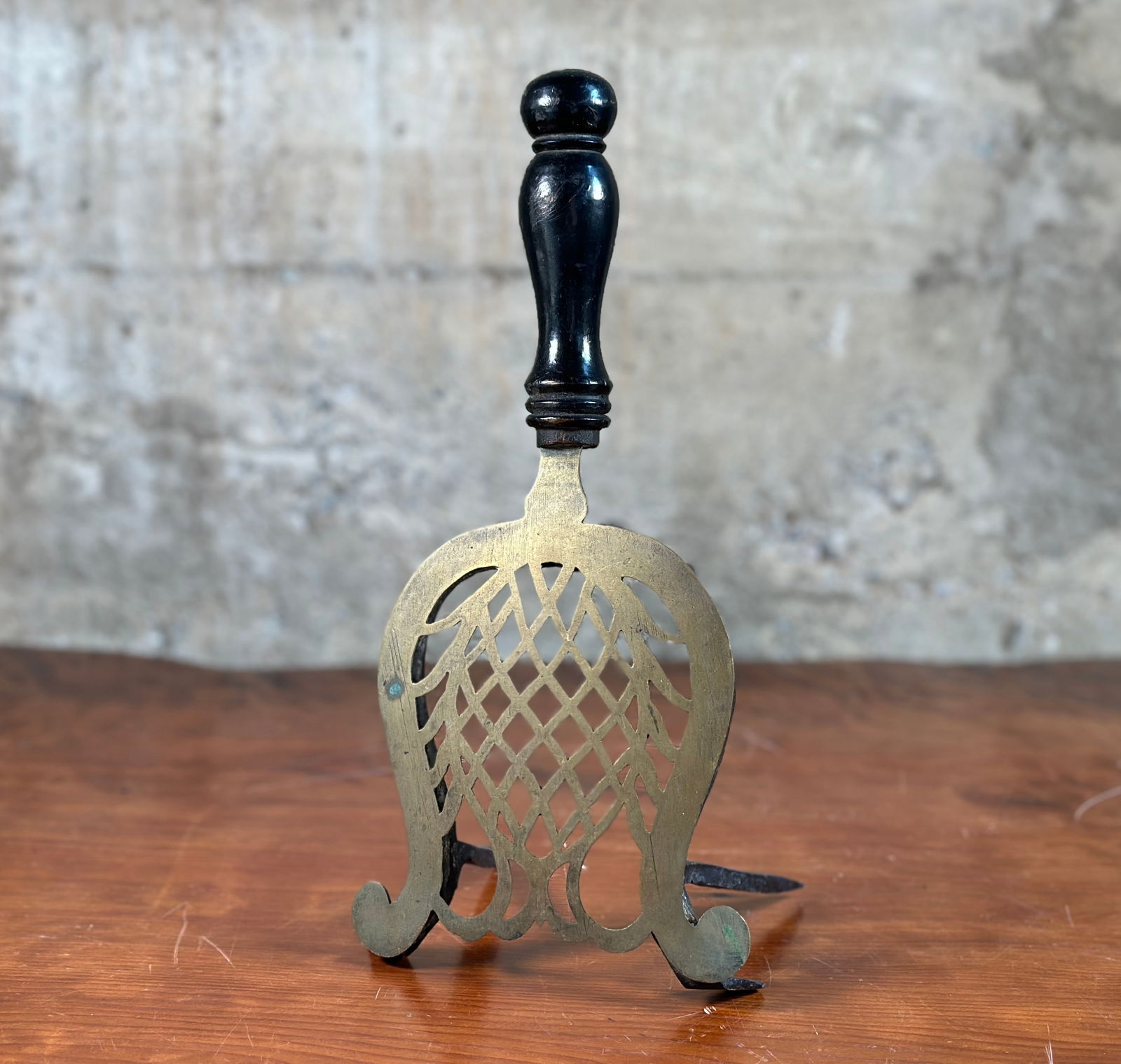 ENGLISH BRASS TRIVET: An English brass trivet featuring an intricately designed top and a smooth wooden handle. Originally used in a hearth/fireplace, it is perfect for resting hot pots and pans, also useful for potted pla