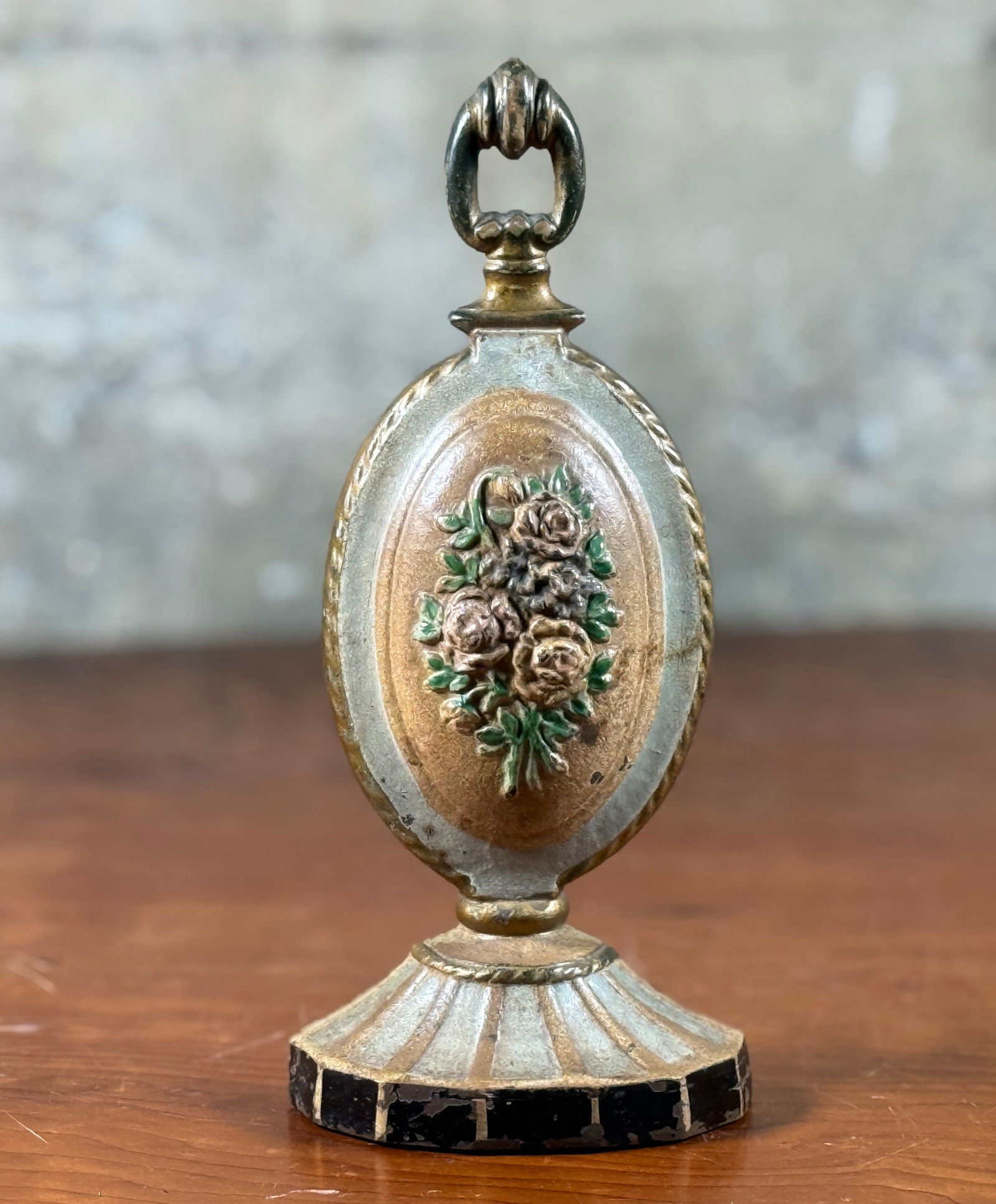 CAST IRON DOORSTOP WITH ROSE MEDALLION DESIGN: This lot features a cast iron doorstop featuring a rose medallion design. The doorstop consists of an oval central medallion with pink and yellow roses, green leaves, and blue flowers on a yellow back