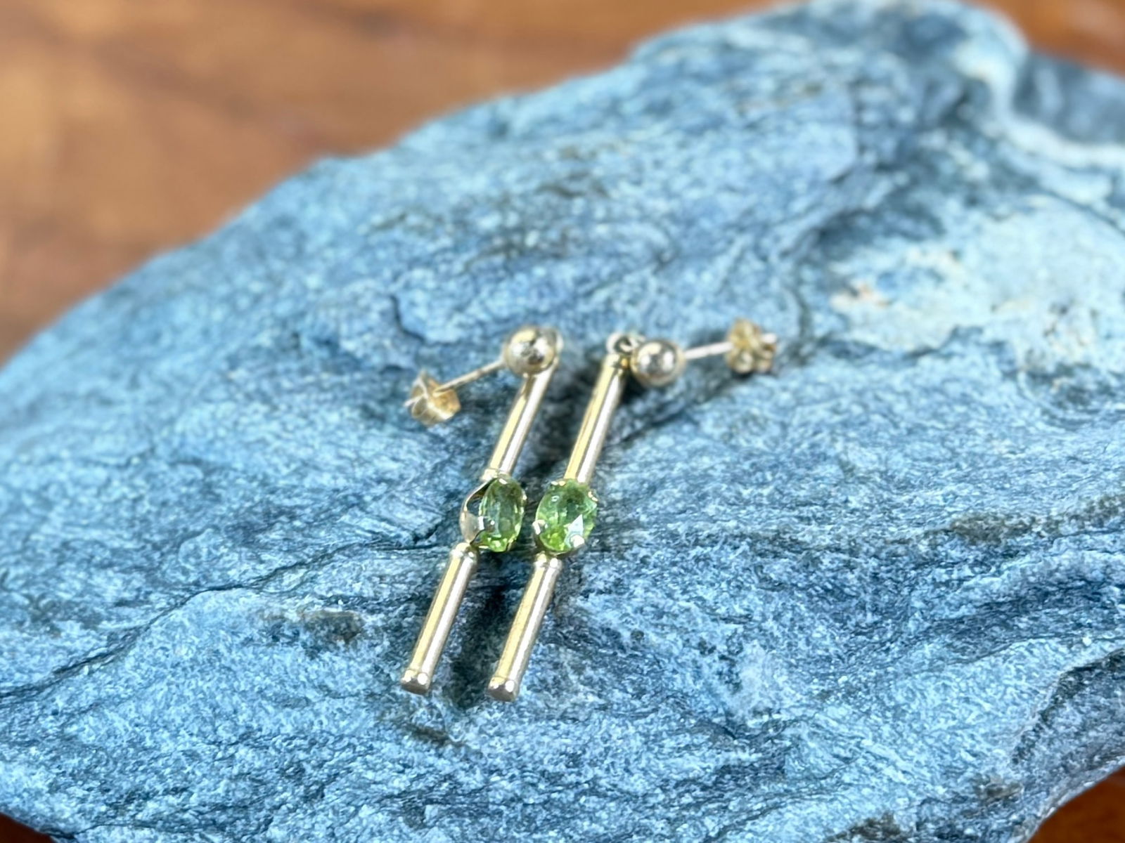 14K GOLD PERIDOT EARRINGS: This lot features a pair of stunning 14k gold earrings, each with a Peridot stone and a total approx. weight of 1.12 grams.