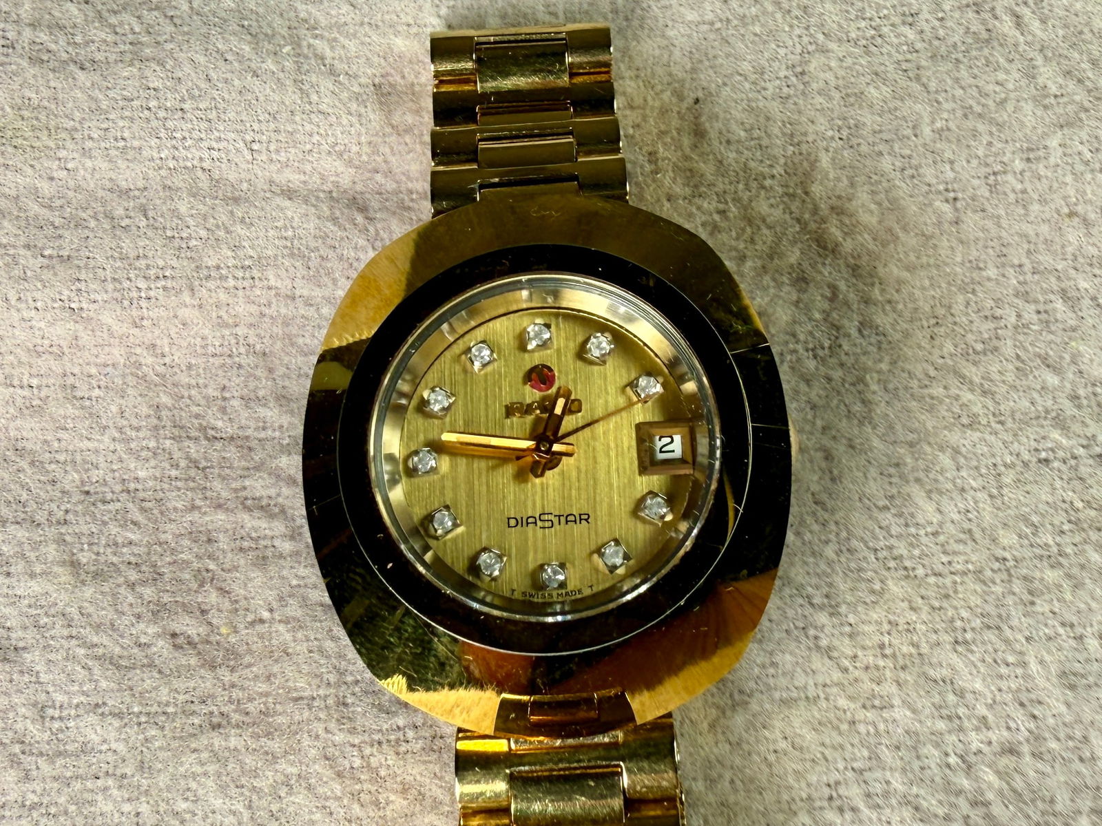 RADO DIASTAR WATCH: This lot features a vintage Rado unisex Swiss DiaStar gold-tone stainless steel watch with a sapphire crystal, diamond accents, and a date window. This is an automatic watch with an unknown service hi