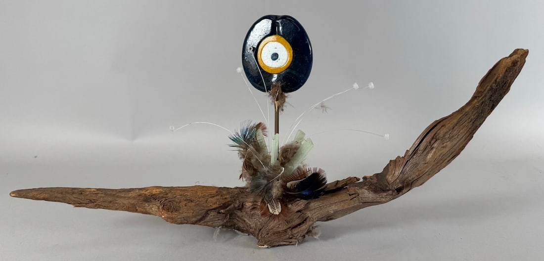 American Indian-Inspired Mixed Media Sculpture with Devil's Eye by Sydney K. Hamburger: Mixed media sculpture decorated with devils eye and bird feathers and wood. D: 8"h x 16.5"w x 3"d.