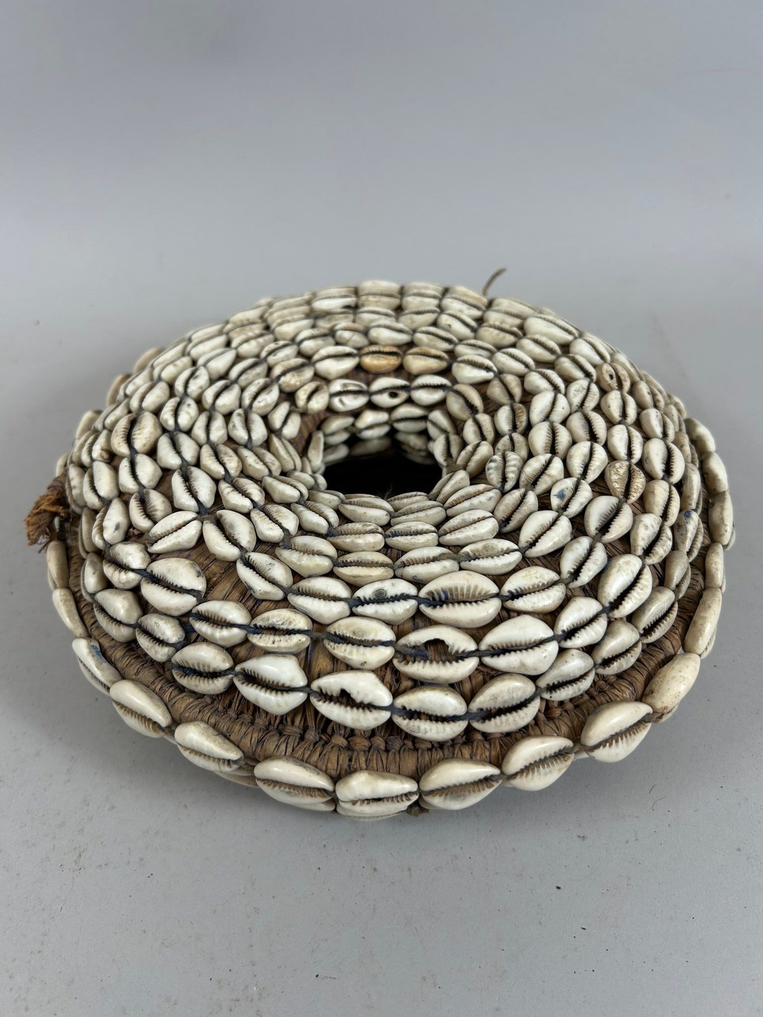 West African Pot Holder: A pot holder, cowrie shells, plant fiber, West Africa. Approximate dimensions: 3" high x 9" diameter