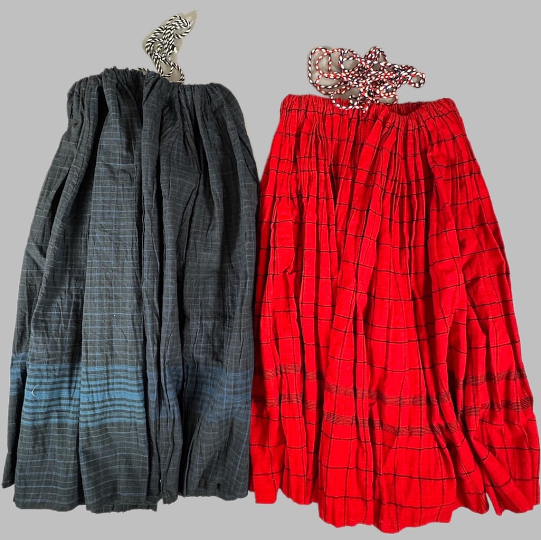 Lot of 2 - Vintage Handmade Plaid Drawstring Skirts Guatemala, Ex Museum: Plaid drawstring skirts in navy blue with light blue stripes and red with black stripes. D: Largest 31.5"L x 186"W, smallest 32.5"L x 136"W. PROVENANCE:From Minneapolis Institute of Art