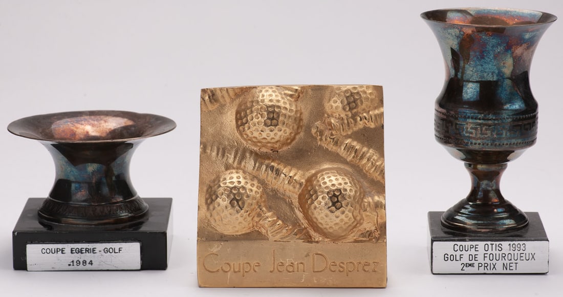 Set consisting of three golf trophies: 1 / Jean Deprez Cup, gilded bronze about golf balls and golf cane. Height 10.5 cm, width 9.5 cm. Work circa 1990.2 / Cup Otis 1993, urn engraved Greek style, black marble base. Height 13 cm.3 / Cup Eg