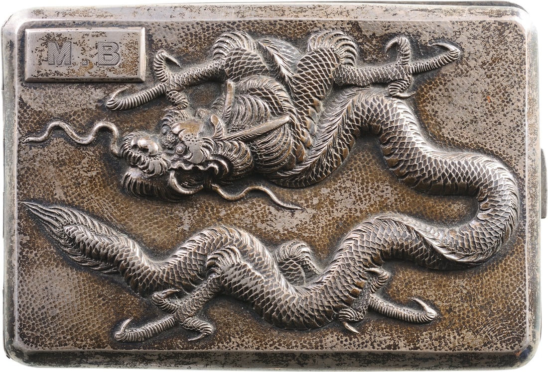 A silver Cigarette box: Of curved shape to better fit in a pocket, the lid embossed with a dragon and a rectangular plate engraved with the initials "M.B.", matted and gilt inner compartment, struck with the "STERLING" mark.