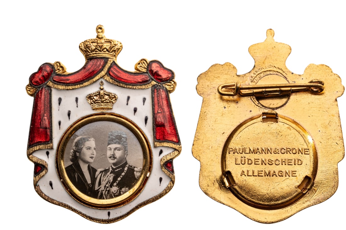 ROYAL MARIAGE BADGE OF KING FAROUK AND QUEEN NARRIMAN SADEK, 1951: Breast Badge, 28x23 mm., gilt Brass, obverse enameled, maker's mark "PAULMANN & CRONE, LUDENSCHEID - ALLEMAGNE", original horizontal pin on reverse. A very rare and attractive badge, of best German je