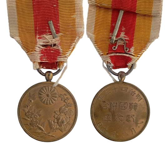 Korea Annexation Medal, 1912: Breast Badge, 36x30 mm, gilt Brass, original suspension ring and worn ribbon. I-